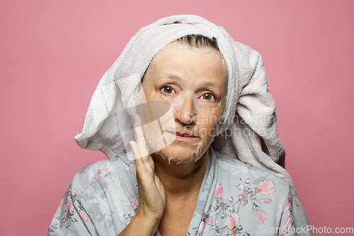 Image of senior woman applying a facial mask napkin