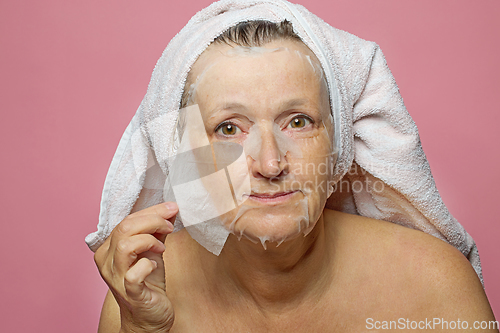 Image of senior woman applying a facial mask napkin