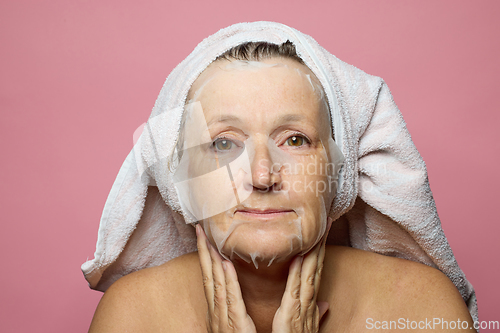 Image of senior woman applying a facial mask napkin