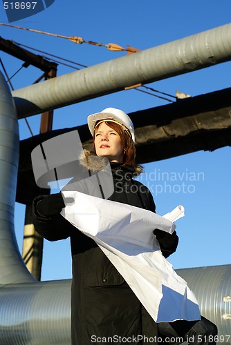 Image of Young architect looking at blueprint in front of construction si