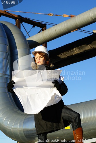 Image of Young architect looking at blueprint in front of construction si