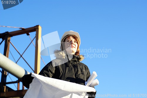 Image of Young architect looking at blueprint in front of construction si