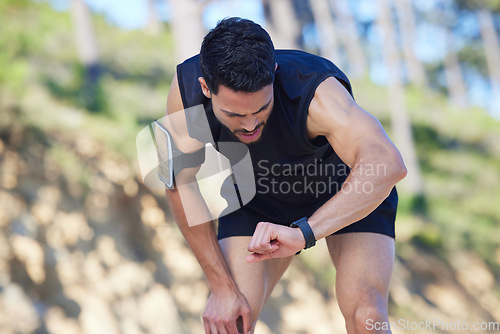 Image of Exercise, watch and time with a sports man tracking his fitness on a sport app while running outdoor in nature. Training, workout and health with a male athlete timing his run, speed or distance