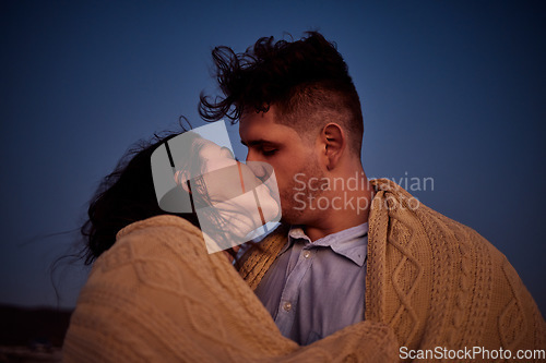 Image of Kiss, love and winter with a couple at night in a blanket for romance, date or anniversary with a dark blue sky. Kissing, dating and honeymoon with a young man and woman sharing an intimate moment