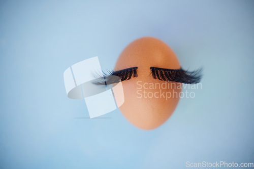 Image of Beauty, makeup and eyelashes with an egg on a blue background in studio with mockup. Cosmetics, mascara or abstract with an embryo and fake lashes with product placement for marketing or advertising