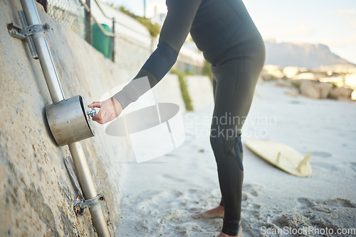 Image of Beach, surfer man and shower after surfing by ocean to clean surfboard on holiday, vacation or summer trip. Surf, washing and hygiene of male at sandy seashore in Canada for water sports or exercise.