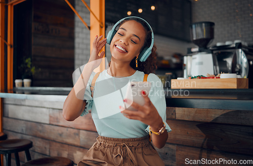 Image of Phone, music and coffee shop with a woman customer streaming audio on headphones in her local internet cafe. Mobile, radio and 5g with a young female using a subscription service in a restaurant