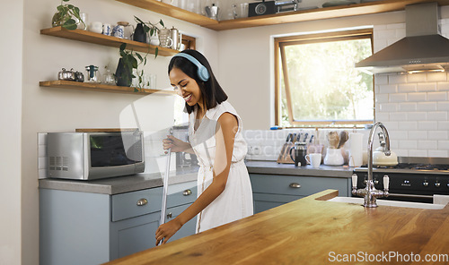 Image of Happy, headphones and woman cleaning the kitchen while listening to music, podcast or radio. Happiness, smile and girl cleaner or housewife washing the floors in a modern home, house or apartment.