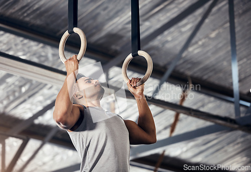 Image of Fitness, exercise man in gymnastics gym during pull up, training or exercise on rings. Young sports athlete or gymnast, strong mindset and start workout to improve muscle or cardio at sport club