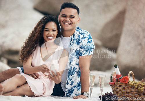 Image of Couple, phone and beach picnic date with champagne, food basket and fruit for anniversary celebration, valentines day or love bonding. Portrait, smile or happy woman with relax man and 5g mobile tech