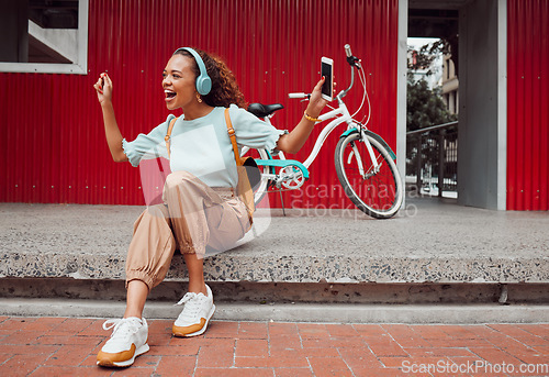 Image of Black woman in city, listen to music on headphones and relax on street sidewalk waiting for a taxi. Girl streaming podcast, musician online and happy dance song from smartphone 5g internet connection