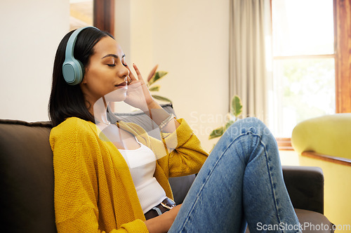 Image of Woman, music and relax with headphones on living room sofa enjoying calm relaxation at home. Young female relaxing on a couch listening to calming audio track at the house for stress relief