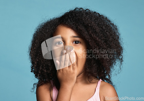 Image of .Black child, surprised and shocked with wow expression covering mouth in awe feeling positive and excited with natural afro hair. Face portrait of cute kid amazed and happy against blue background.