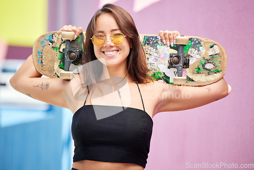 Image of Happy, city and portrait of a woman with skateboard outdoor in the urban road while on holiday. Happiness, sunglasses and girl skater from Singapore with a smile standing in town street on adventure.