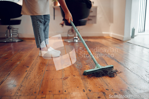 Image of Hairdresser woman, sweeping hair and cleaning salon or barbershop wooden floor after cutting a hairstyle or doing a trim. Feet of female worker with broom for dirt, dust and mess for clean workplace