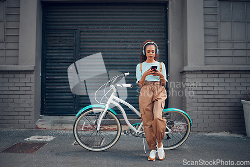 Image of Headphone, woman and phone with bicycle in city listening to music or podcast streaming outdoor in summer with trendy look. Eco friendly transportation for carbon footprint bike using 5g network