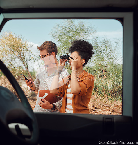 Image of Window, car and diversity couple on road trip journey to explore Australia safari, countryside or outdoor nature. Binocular, transportation adventure and man streaming football game on mobile phone