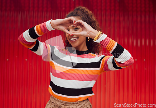 Image of Heart shape, hands and portrait of a happy woman in a studio with trendy, stylish and fashion clothes. Happiness, smile and love gesture with girl model from Puerto Rico standing by a red background.