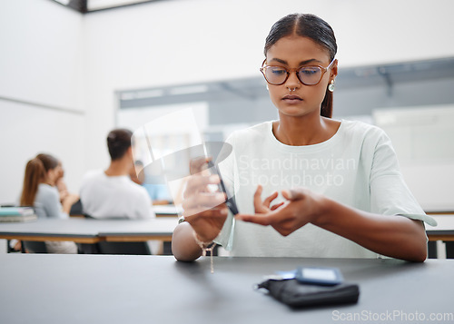Image of Diabetes, finger prick and black woman with blood sugar test to check glucose level sitting at desk in class. Sick and diabetic female student using glucometer pen for control and healthcare