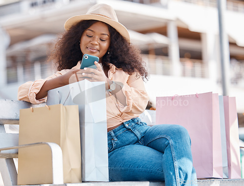 Image of Phone, shopping and happy black woman with shop and store bags on a bench outdoor. Online, mobile and ecommerce app scroll of a young person smile from Miami with technology and retail paper bag
