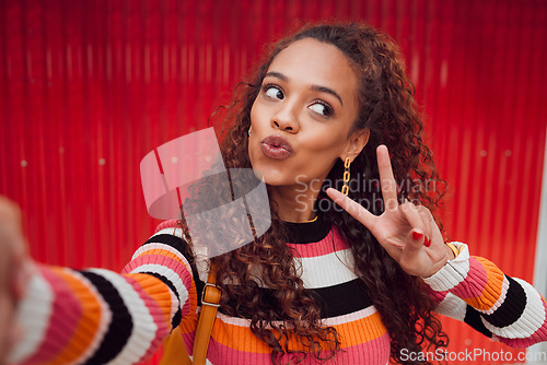 Image of Fashion selfie, peace sign and happy woman against a red wall in city for fun travel holiday. Portrait urban girl show cool hand gesture and lips while traveling and sharing picture on social media