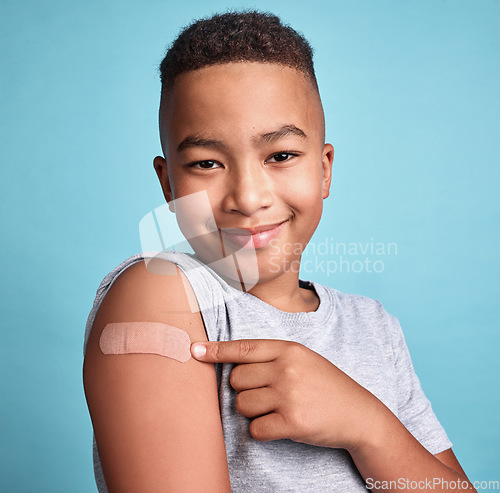 Image of .Child black, band aid and happy kid with vaccine, in blue studio background and relax with smile or joyful. Portrait, boy and adhesive bandage with arm bruise, confident and vaccination for health.