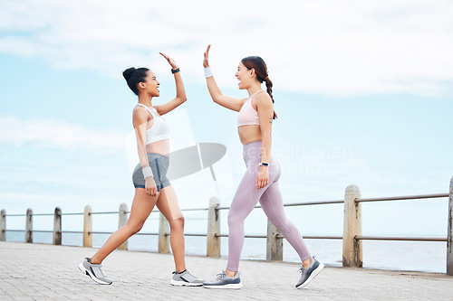 Image of Fitness, friendship and high five, women on running path at the ocean for motivation, support and friends to workout together. Health, wellness and partnership success for girl and personal trainer.