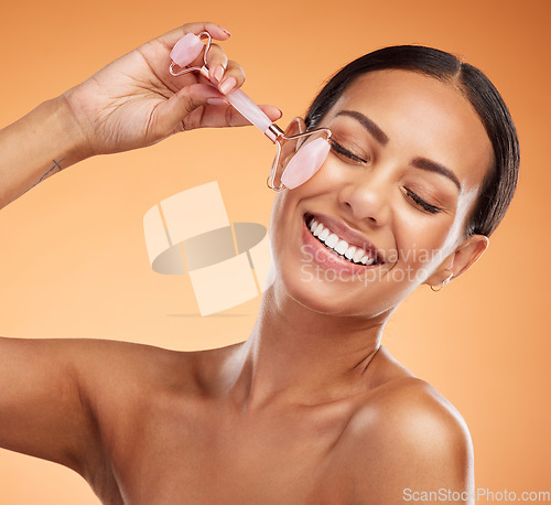 Image of Jade roller, skincare and woman with massage for face beauty against an orange studio background. Happy, young and healthy model with a dermatology product for facial wellness and care with a smile