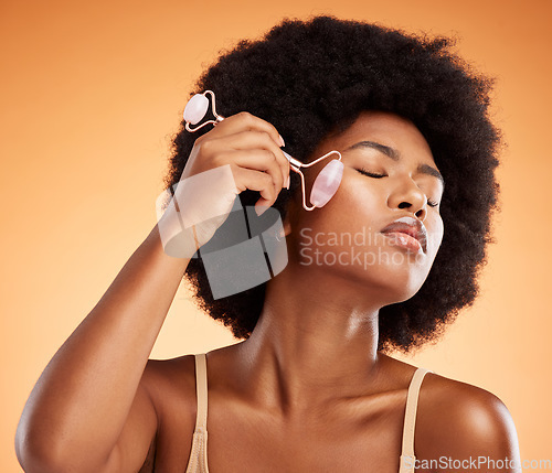 Image of Beauty, afro and black woman with skincare derma roller for healthy and natural skin on face. Wellness and massage girl satisfied with rose quartz self care treatment with orange background.