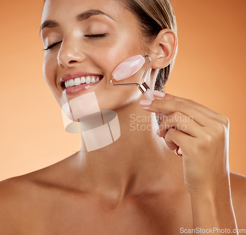 Image of Skincare, cosmetics and woman with face roller, natural beauty and glow with confidence, smile and firm or anti aging in brown studio background. Makeup, girl or body care, wellness or facial massage