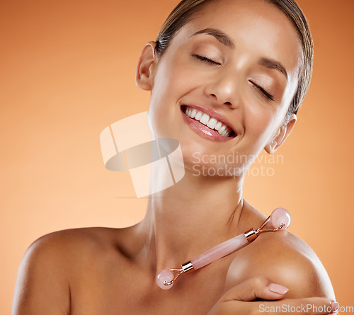 Image of Woman beauty, face massage and rose quartz roller, skincare cosmetics product or glowing makeup tool on grey studio background. Smile, happy and healthy lady model, wellness and natural selfcare