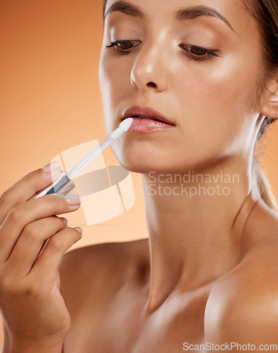 Image of Beauty, makeup and lip gloss with woman in a studio for grooming, hygiene and lips cosmetics. Face, skincare and model apply lipstick against a brown background for full, feminine and natural lip