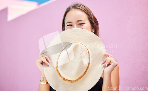 Image of Travel, fashion and summer hat with a woman tourist in the city on a pastel color pink wall background. Happy, holiday and tourist with a female traveler covering her face with a sunhat in town