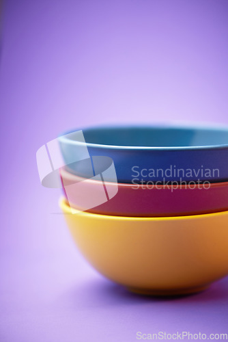 Image of Color, container and group of ceramic bowl, kitchen equipment or plastic plate tower for soup, cereal or breakfast food. Colorful stack of blue, yellow and maroon objects on purple background studio