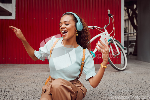 Image of Headphones, music and happy woman singing in the city while streaming audio or radio online. Happiness, excited and girl from Puerto Rico listening to a track while sitting on pavement in urban town.