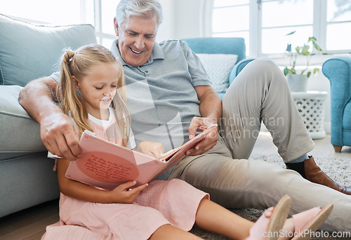 Image of Book, family and children with a girl reading to her grandfather on the floor of their living at home. Kids, read and story with a senior man and granddaughter bonding in their house during a visit