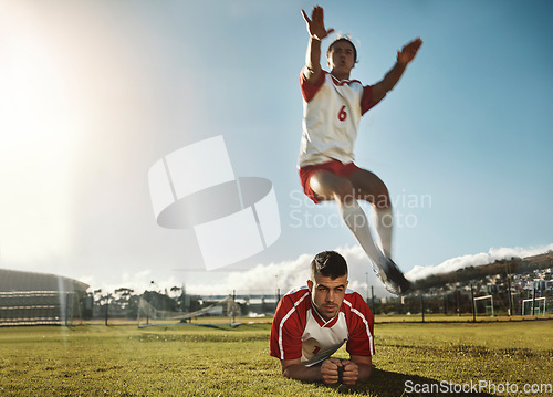 Image of Soccer, fitness and training with a sports man jumping over his teammate during practice on a grass pitch or field. Football, workout and exercise with a male athlete exercising with his team outdoor