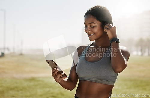 Image of Black woman, music earphones or phone for fitness podcast, exercise motivation or training radio on sports grass field. Smile, happy and mobile technology for athlete or workout health data on 5g app