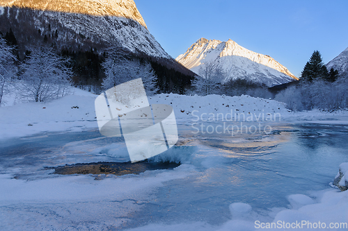 Image of A frozen river with snow and mountains in the background