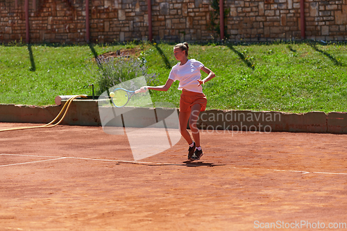 Image of A young girl showing professional tennis skills in a competitive match on a sunny day, surrounded by the modern aesthetics of a tennis court.