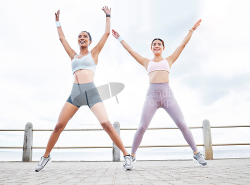 Image of Jumping jack, fitness and women training cardio, happy with workout and smile during exercise in the city by the ocean. Young friends with energy for sports collaboration and stretching in the street