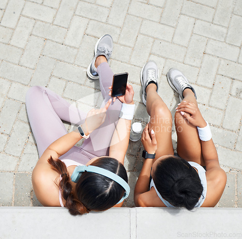 Image of Women in city, online workout app in Miami and healthy friends relax sitting on urban floor watching fitness video. Girl streaming audio podcast, show social media exercise and outdoor 5g technology