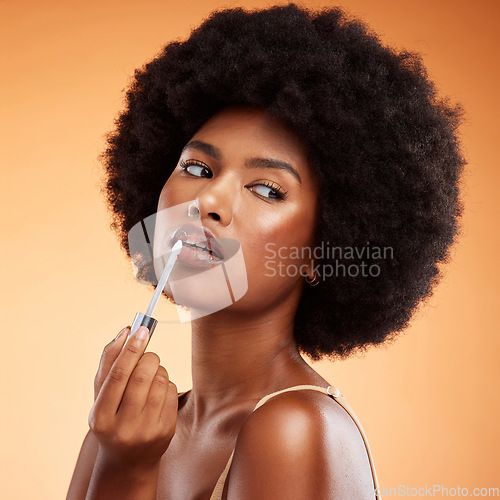 Image of Black woman, afro and natural beauty lip gloss treatment for a healthy, shiny and transparent tint. Cosmetics, apply and beautiful face of African model holding makeup tool at orange background.