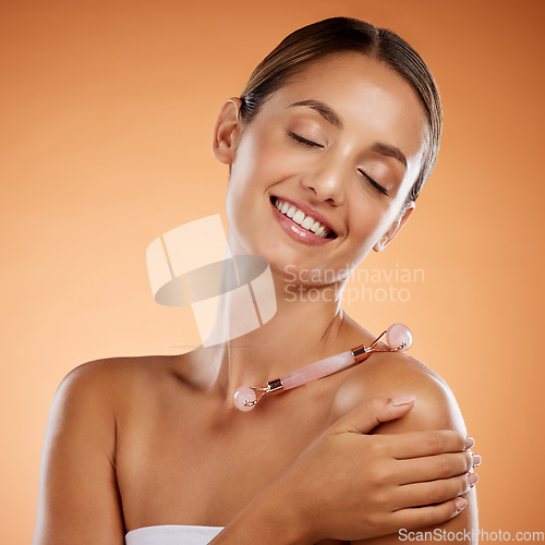 Image of Cosmetics, woman and face roller for natural beauty, skincare and smile with brown studio background. Makeup, body care and confident girl being happy, with smooth skin and dermatology wellness.