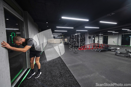 Image of A muscular man is focused on working out with dumbbells in a modern gym, showing his determination and commitment to his fitness regimen.