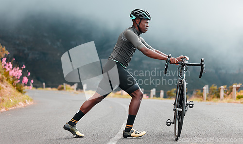 Image of Stretching legs, fitness and man cycling on a road with a bike in the mountains for cardio, travel and sports workout in nature. Athlete doing a warm up before training on a bicycle in the street