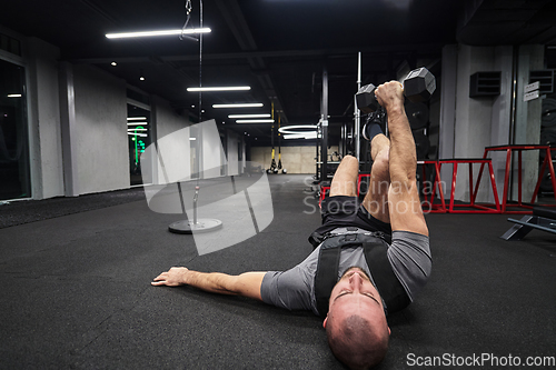 Image of A muscular man is focused on working out with dumbbells in a modern gym, showing his determination and commitment to his fitness regimen.