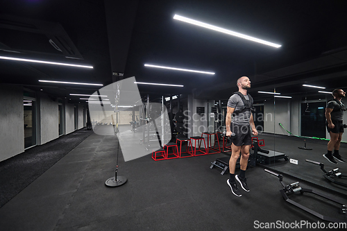 Image of A muscular man is focused on working out with dumbbells in a modern gym, showing his determination and commitment to his fitness regimen.