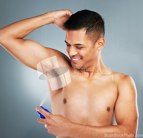 Image of Happy, smile and man with deodorant spray for hygiene, fresh scent and fragrance after a shower. Happiness, clean and guy spraying his armpit to prevent odor or smell isolated by a gray background.