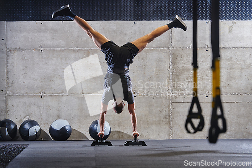 Image of A muscular man in a handstand position, showcasing his exceptional balance and body control while performing a variety of exercises to enhance his overall body stability and strength in a modern gym